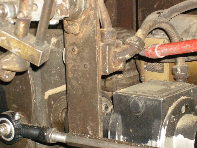 Eine stark verschmutzte Brotverpackungsmaschine vor der Reinigung mit Trockeneisstrahlen. Überall an der Maschine sind Rückstände und Staub sichtbar. Metallische Komponenten, Förderbänder und andere Maschinenteile sind von einer dicken Schicht Schmutz bedeckt.