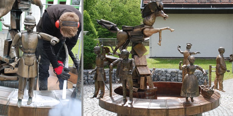 Zweiteiliges Bild: Links ist ein Dienstleister mit Gehörschutz und roten Handschuhen zu sehen, der eine Bronzestatue mit einem Trockeneisstrahlgerät reinigt. Rechts wird die gereinigte Bronzeskulpturengruppe gezeigt, die detailreiche Figuren, darunter einen Soldaten, eine Frau im traditionellen Kleid und ein Pferd mit Reiter, darstellt. Die Skulpturen stehen auf einem Amtsschimmelbrunnen in einer grünen Außenanlage.