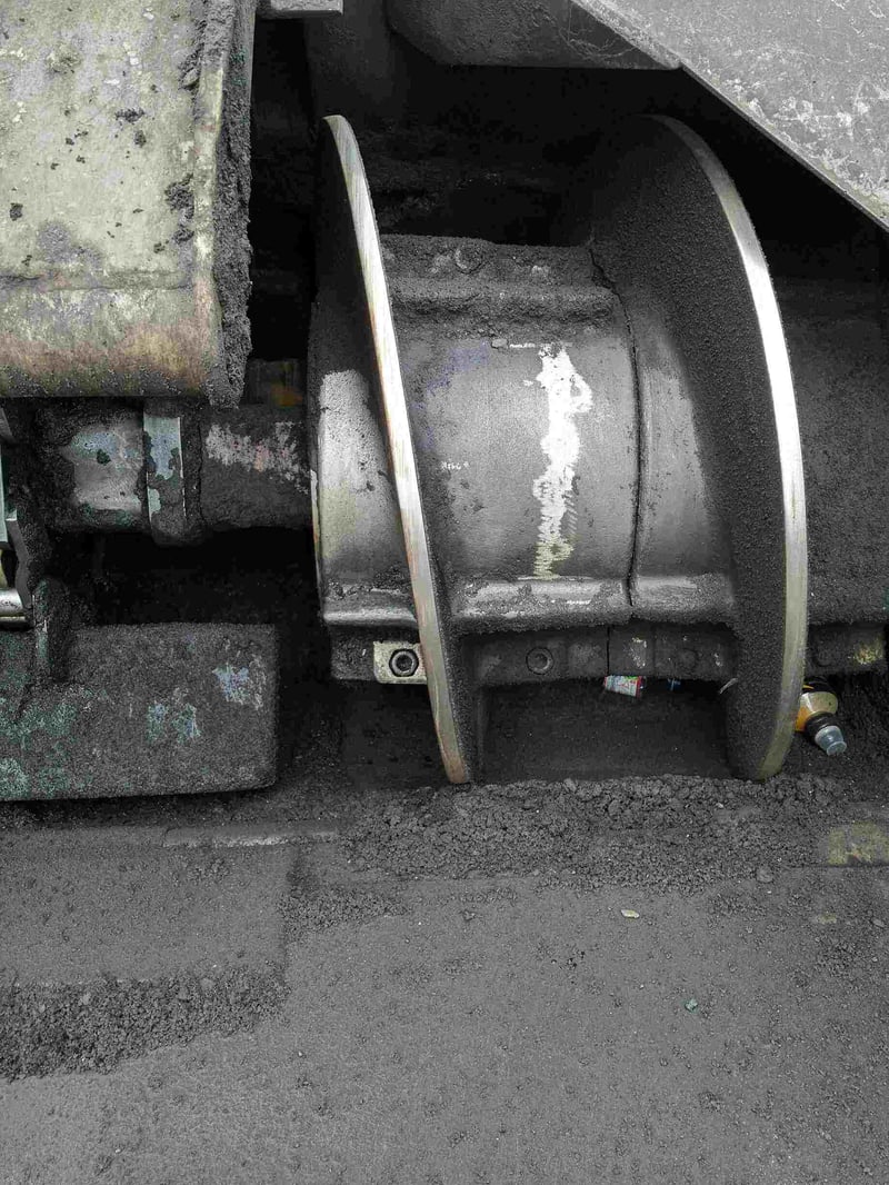 Nahaufnahme einer Förderschnecke oder eines Verteilerelements einer Asphaltmaschine nach der Trockeneisreinigung. Die Metalloberflächen sind nun deutlich sichtbar, sauber und glänzend, obwohl noch einige sehr feine Asphaltreste in den Ritzen oder an den Kanten zu erkennen sind. Der Großteil des ehemals dicken Belags wurde entfernt, und die darunterliegende Maschinentechnik tritt klar hervor.