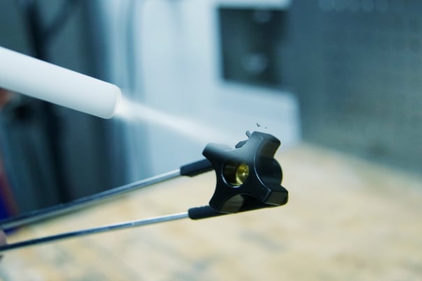 Nahaufnahme einer Trockeneisstrahlung zur Entgratung eines Kunststoffteils. Eine Düse sprüht Trockeneis präzise auf das Werkstück, während dieses mit einer Haltevorrichtung fixiert wird, um überschüssiges Material schonend zu entfernen.